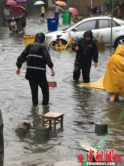 大雨中，城管队员帮助市民寻找积水中的漂浮物。 城管供图