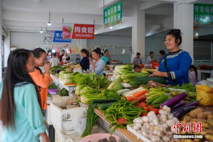 贵州省榕江县易地扶贫搬迁安置点卧龙小区，侗族妇女石本艳(右一)在菜市场卖菜。中新社记者 贺俊怡 摄